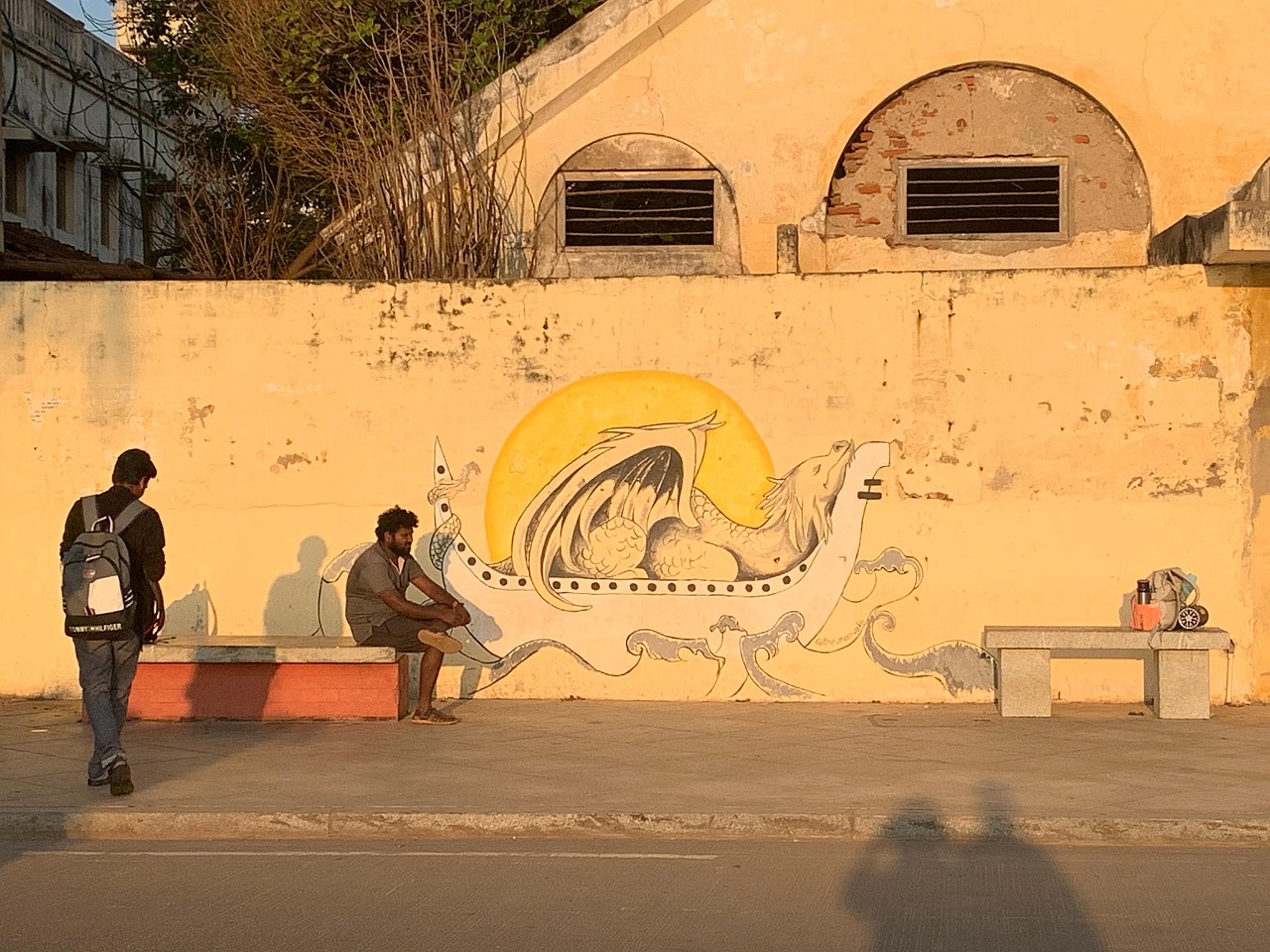 A White Town street at golden hour — ochre colonial wall with mural, locals resting on a bench.